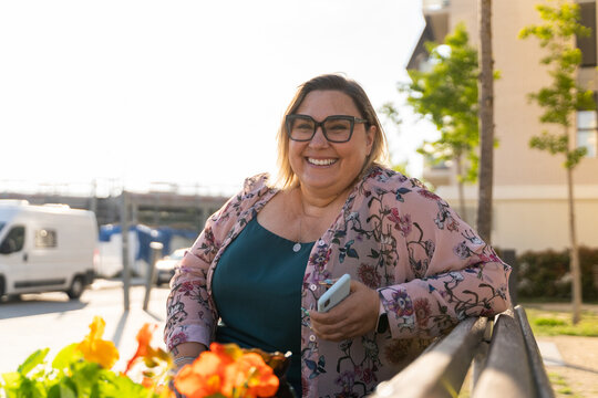 Smiley woman sitting in bench in park with phone