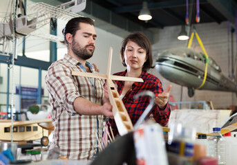 Female and male hobbyists engaged in creating plane models in aircraft workshop..