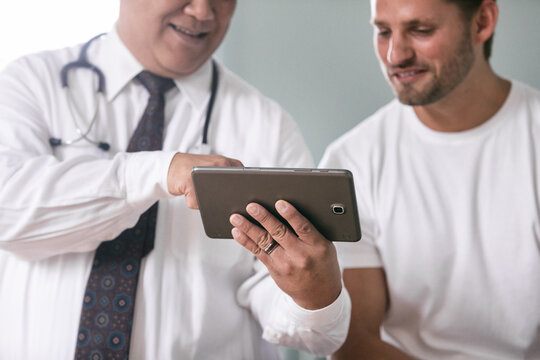 Exam: Doctor And Man Look At Digital Tablet