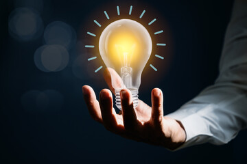 Man hold lightbulb with glowing effect as creativity on dark blue background. Idea and knowledge for innovation