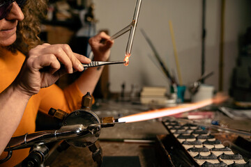 Close up of woman lampworker using tongs to manipulate hot glass tubes