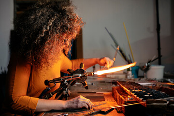Side view of a woman lampworker working with torch flame and glass pipe