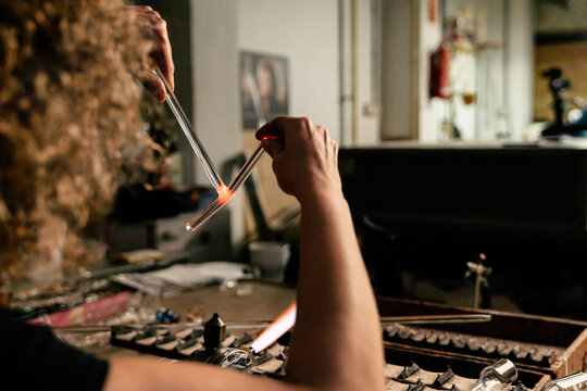 Woman glassblower holding two glass tubes and joining them together with heat