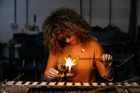 Front view of woman lampworker working with tongs and glass tubes with the torch flame