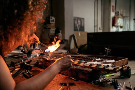 Woman glassblower holding and joining two glass tubes together with the torch flame
