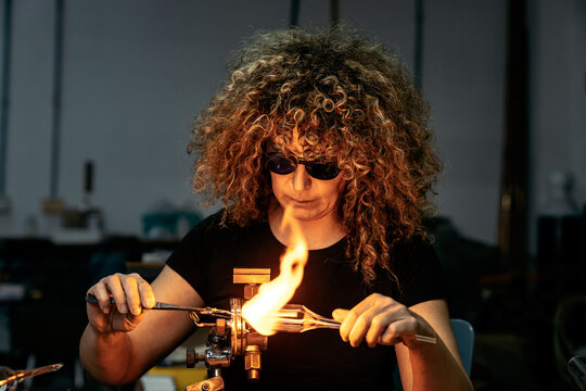 Glassblower adult female working with torch flame and glass pipe