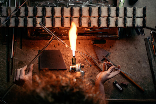 High angle rear view of woman lampworker working with glass tubes with the torch flame