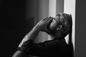 Black and white portrait of depressed young man in dark room