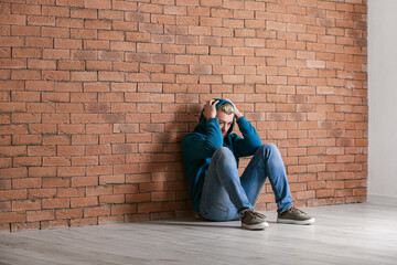 Depressed young man sitting near brick wall