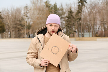 Non-binary young man holding cardboard with symbol of bigender outdoors