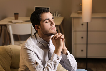 Young man praying at home in evening