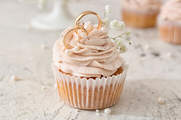 Tasty cupcake and wedding rings on light background