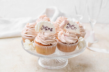 Dessert stand with tasty wedding cupcakes on light background