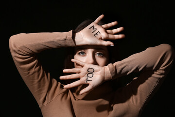 Scared young woman with text ME TOO written on her palms against dark background. Concept of harassment