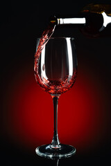 Pouring of red wine into glass on dark background