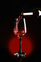 Pouring of red wine into glass on dark background