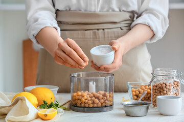 Woman adding salt into blender with chickpeas on table in kitchen, closeup