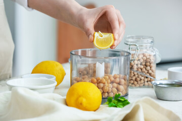 Woman squeezing lemon into blender with chickpeas on table in kitchen, closeup