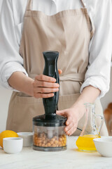 Woman preparing tasty hummus on table in kitchen, closeup