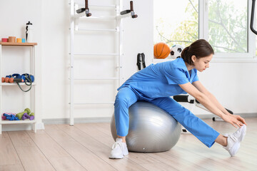 Female physiotherapist demonstrating exercise with fitball in rehabilitation center