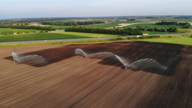 Crop watering agricultural sprinkler in operation next to a highway, drone shot