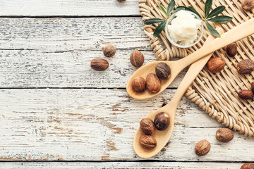 Spoons with shea nuts and butter on light wooden background