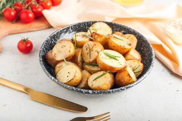 Plate with baked potatoes and rosemary on light background