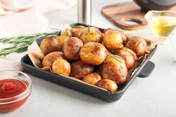 Frying pan with baked potatoes and rosemary on light background