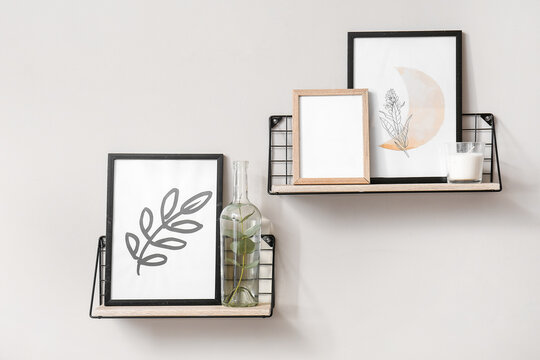 Shelves with stylish pictures hanging on light wall