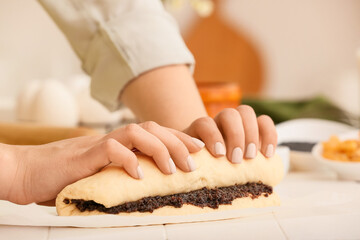 Woman preparing tasty poppy seed bun at table in kitchen