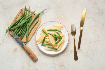 Plate of tasty pasta with green beans on light background