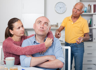 Obraz premium Unhappy family couple hugging after conflict, worried elderly man on backgroud