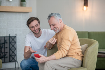 Young man explaining his dad how to use a new smartphone