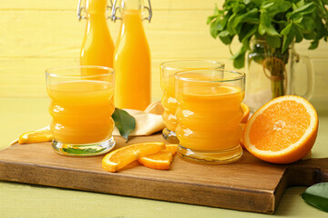 Board with glasses of tasty orange juice on color background