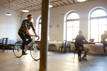 Casual businessman riding bicycle in open office