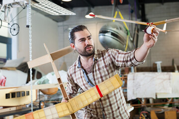 Portrait of happy male hobbyist with monoplane models he created in aircraft workshop..