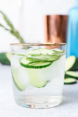 Glass of cold gin tonic and cucumber slices on light background