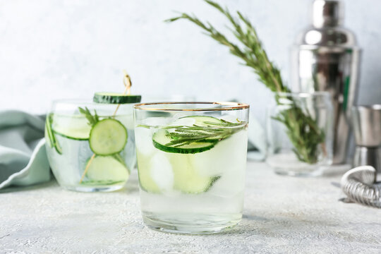 Glass of cold gin tonic and cucumber slices on light background