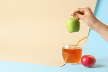 Glass of tasty juice and female hand with apple on color background