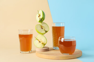 Glasses of tasty juice and apples on color background