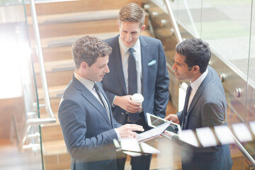 Businessmen with digital tablet and coffee talking on stairs