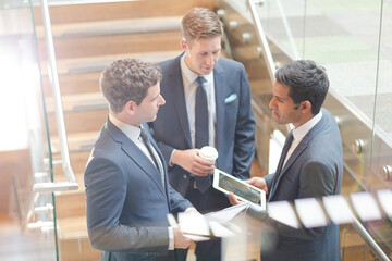 Businessmen with digital tablet and coffee talking on stairs