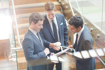 Businessmen with digital tablet and coffee talking on stairs