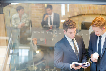 Businessmen discussing paperwork outside conference room meeting