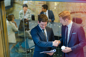Businessmen shaking hands outside conference room meeting