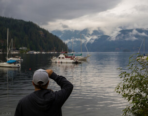 Person look at the calm water, wait yacht in the harbor. Rainy day, fog, mountain forest and ocean...