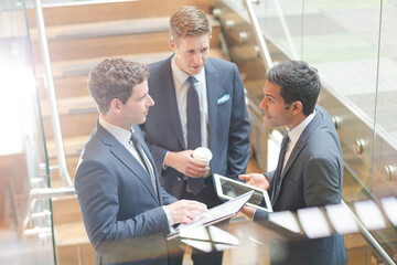 Businessmen with digital tablet and coffee talking on stairs