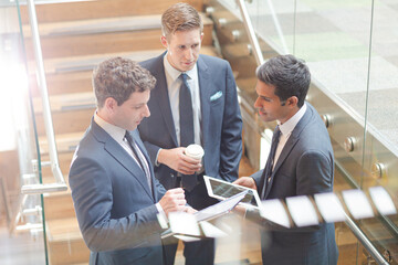 Businessmen with digital tablet and coffee talking on stairs