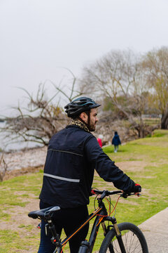 young latino hispanic man walking in a park next to the beach with his bike in the cold morning, vertical photo