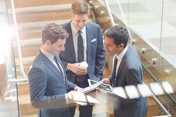 Businessmen with digital tablet and coffee talking on stairs